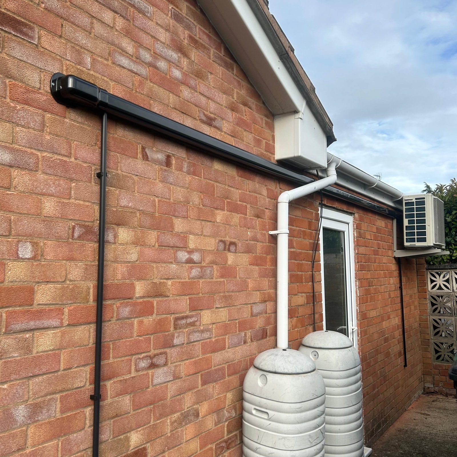 Outdoor condenser unit and pipework installed to the side of a brick house
